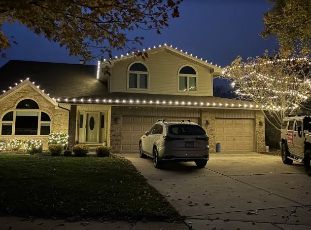 Two-story home with warm white lights tracing every roofline above the driveway
