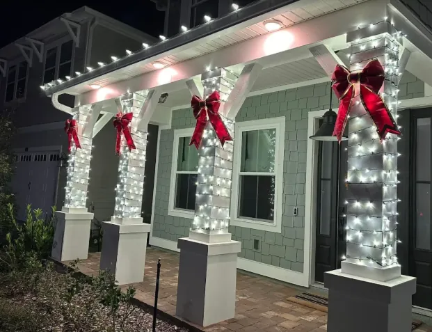 Porch columns wrapped in white lights and topped with red velvet bows