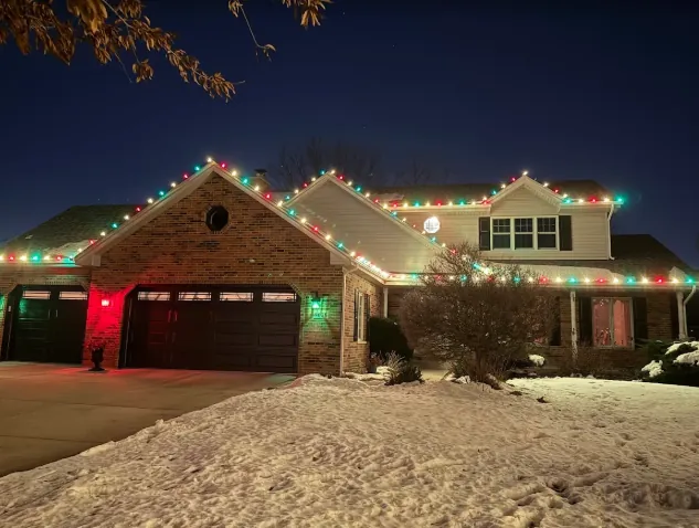 Brick ranch with red and green roofline lights after a snowfall