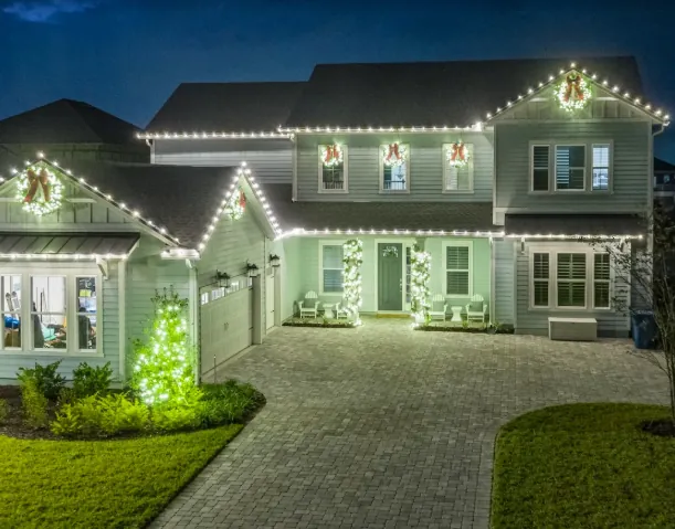 Two-story home with warm white roofline, wreaths, and lit entry columns