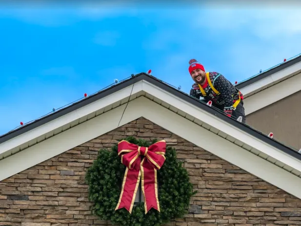 Installer on the roof hanging a large red-bow wreath over the entry