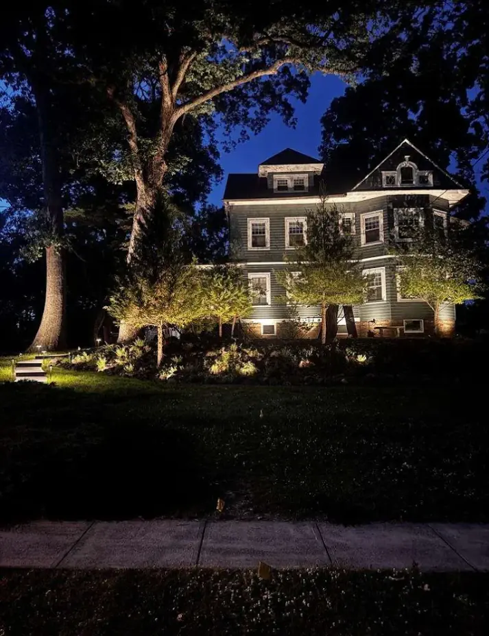 Victorian home at dusk with landscape uplighting on the front trees and garden beds