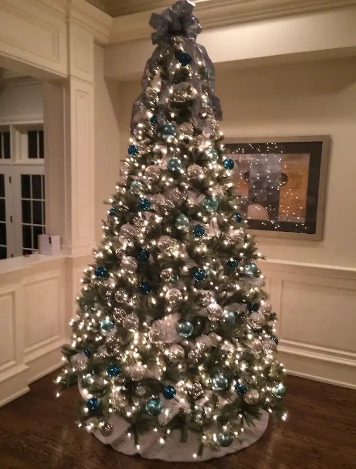 Indoor Christmas tree in warm white lights with blue and silver ornaments and a ribbon topper