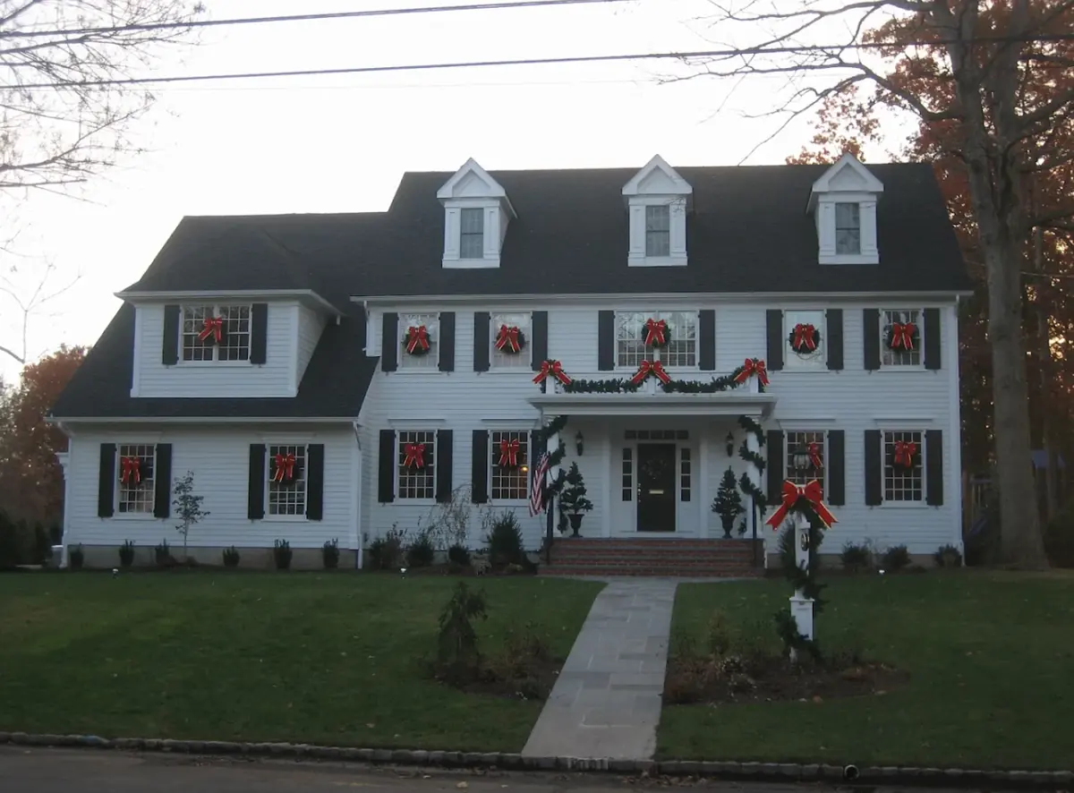 White colonial with a red-bow wreath in every window and garland around the front porch