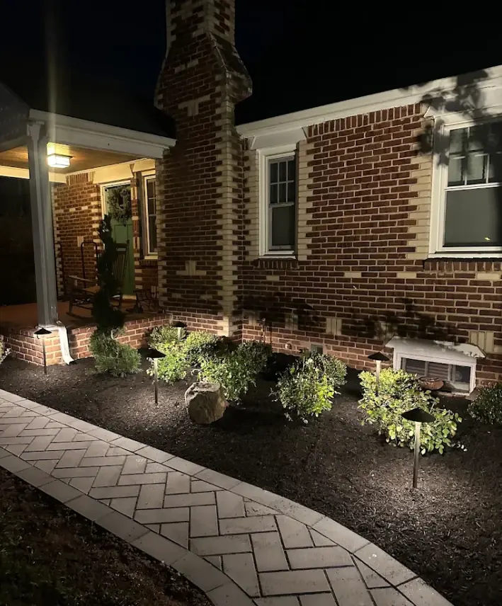 Brick home with low path lights in the front garden bed along a paver walkway