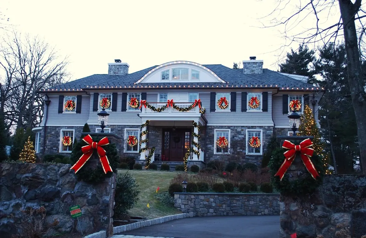 Stone and shingle home with red-bow wreaths in every window and oversized bows on the entry pillars