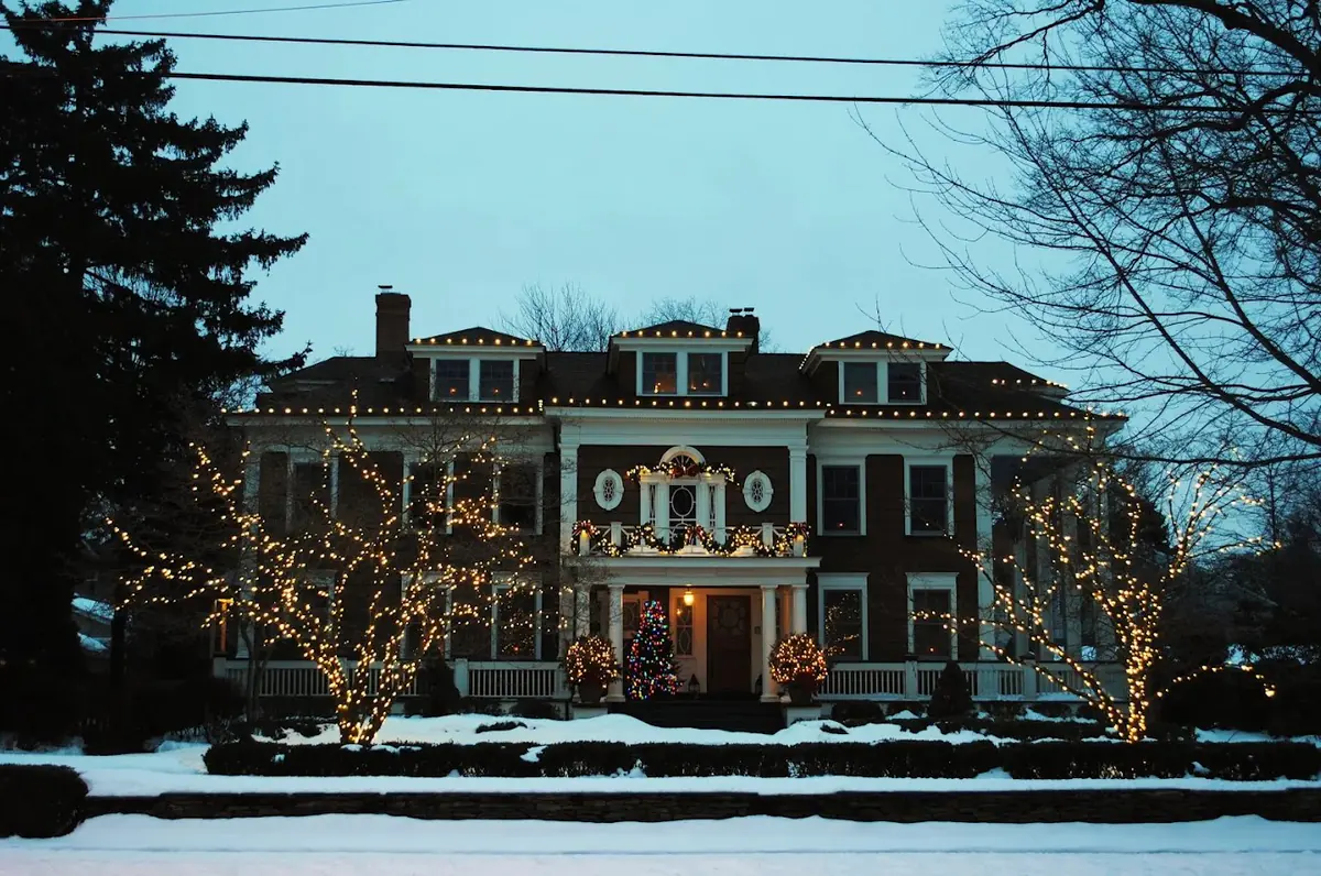 Georgian colonial in the snow with wrapped front trees, roofline bulbs and balcony garland