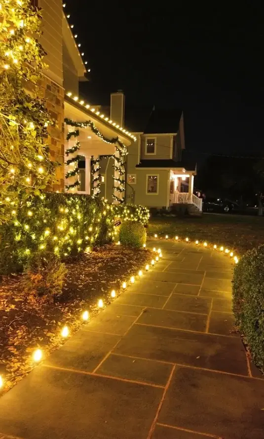 Bluestone walkway lined with C9 stake lights leading to a garland-wrapped porch