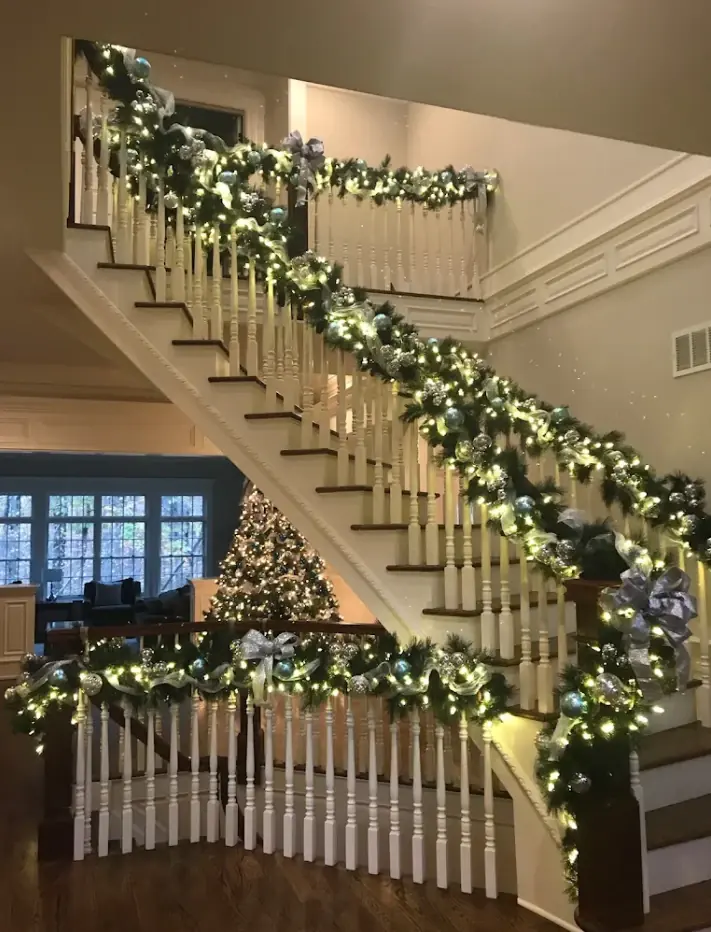 Grand staircase banister wrapped in lit garland with blue and silver ribbon and ornaments