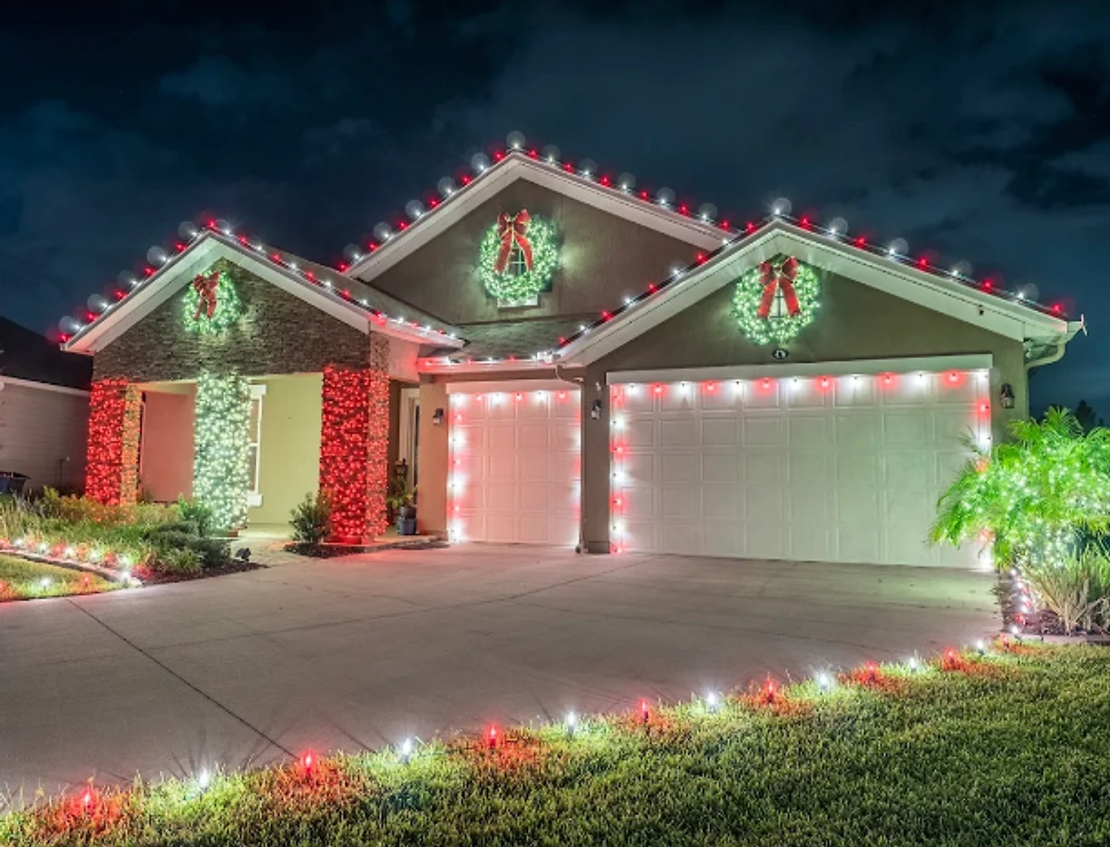Ranch home with red and white roofline lights, wreaths over the garage, and a lit walkway and driveway